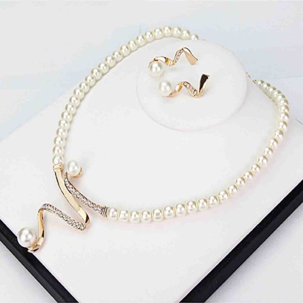 A jewelry set consisting of a white pearl necklace and earrings in gold color on a black background.